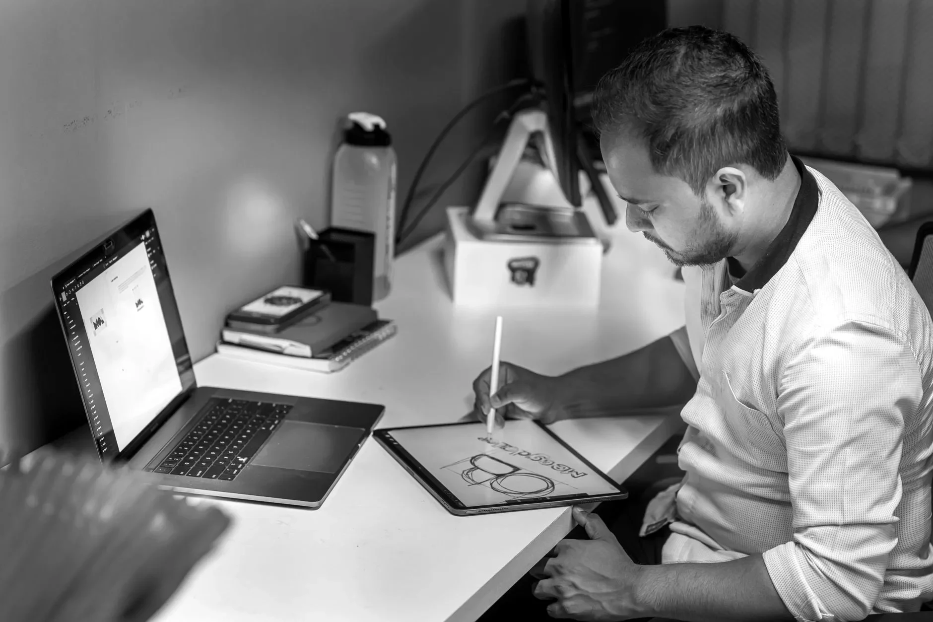 A designer sketching a logo concept on a tablet beside a laptop