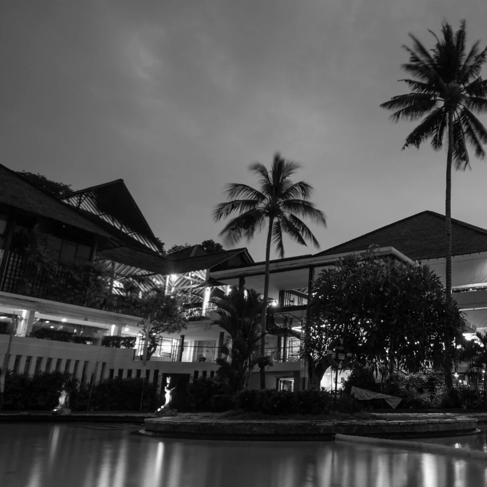 A lit resort building and palm trees reflected in a pool at dusk