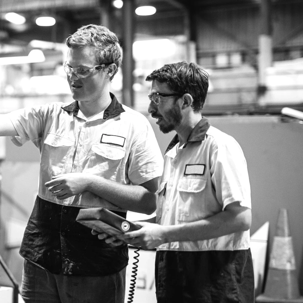 Two technicians in high-visibility shirts inspecting equipment on a factory floor