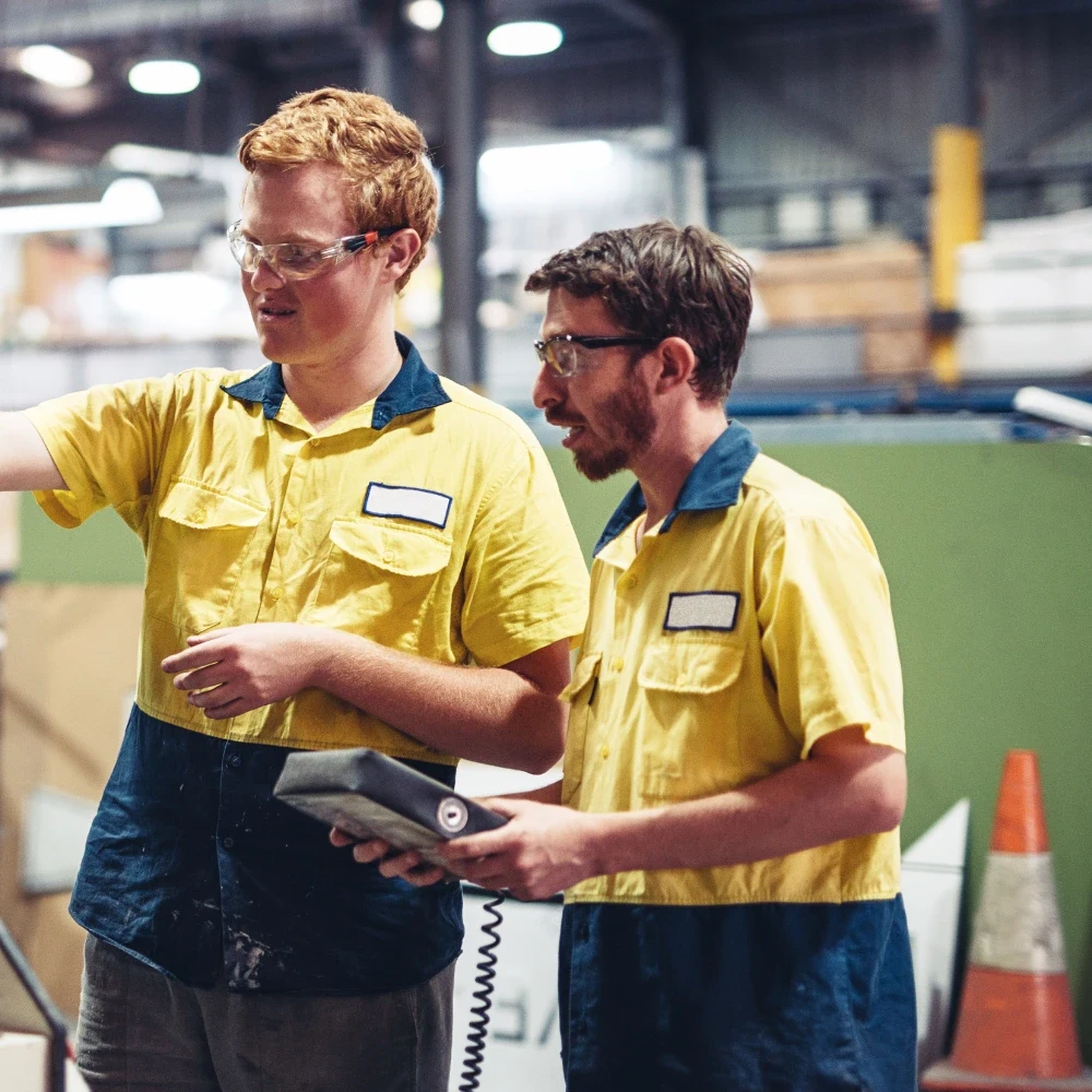 Two technicians in high-visibility shirts inspecting equipment on a factory floor